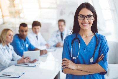 female medical doctor is looking at camera and smiling while her colleagues are sitting