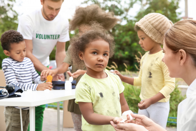 volunteers giving vitamin tablets to poor children outdoors